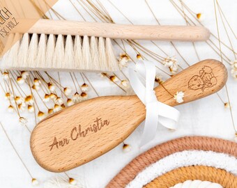 May include: A set of two wooden baby hair brushes. One brush has natural bristles and the other is a soft, oval-shaped brush with the name "Ann Christin" engraved on it. Both brushes have a light wood finish.