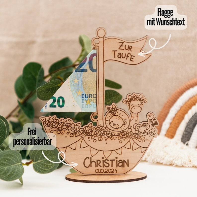 Puede incluir: Portamonedas de madera en forma de velero con una jirafa, un le&oacute;n y un rat&oacute;n. La vela es un billete de 20 euros. El barco tiene una bandera que dice "Zur Taufe" y un nombre y una fecha personalizados. "Christian 01.02.2024".