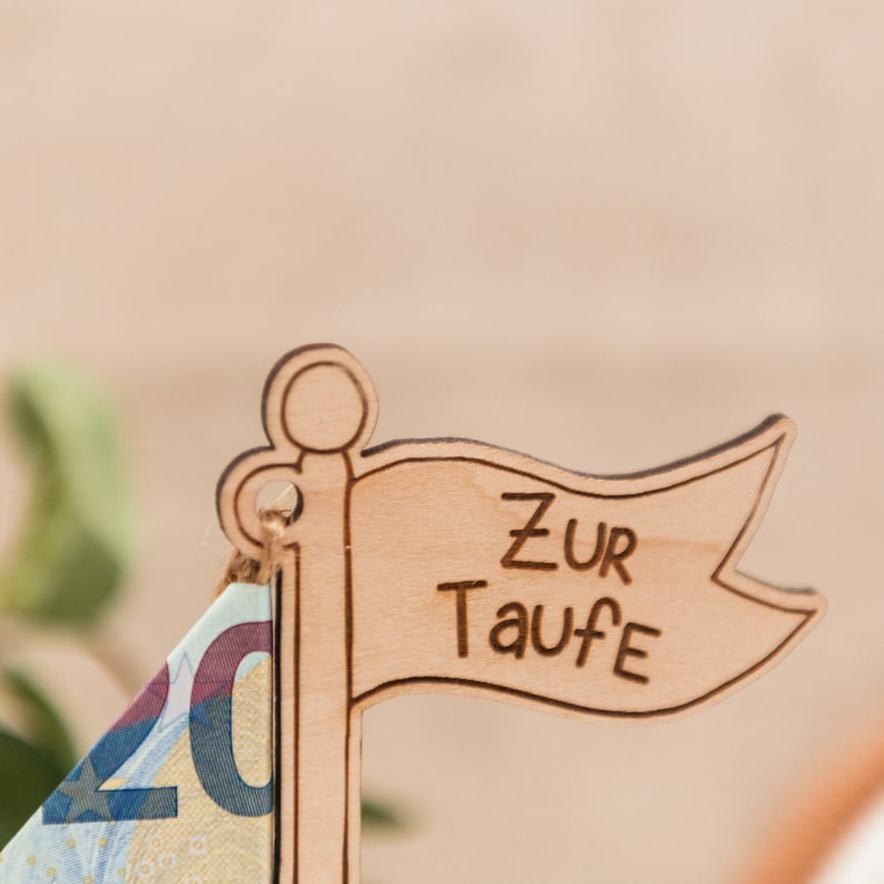 Puede incluir: Un velero de madera con una bandera que dice "Zur Taufe" en alem&aacute;n. El velero est&aacute; decorado con un billete de veinte euros.