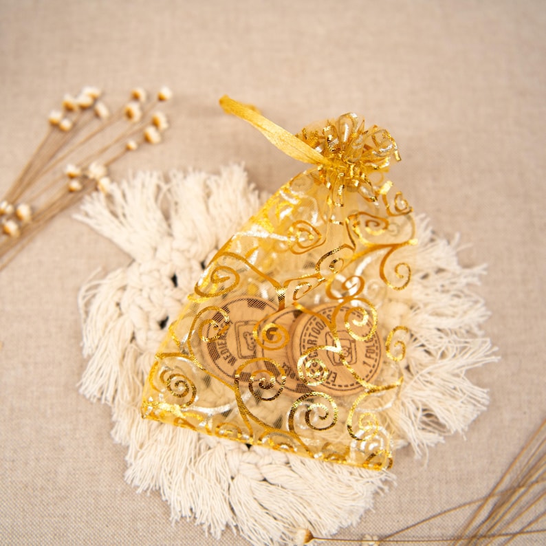 May include: Two round wooden coasters with gold lettering and a gold swirl design. The coasters are in a gold mesh bag with a gold ribbon.