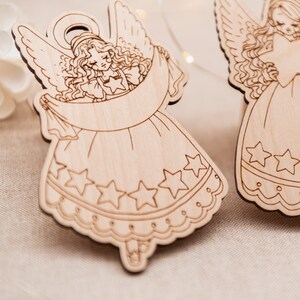 Peut inclure: Deux d&eacute;corations d'ange en bois sur un fond blanc. Les anges tiennent une banni&egrave;re et ont des &eacute;toiles sur leurs robes.