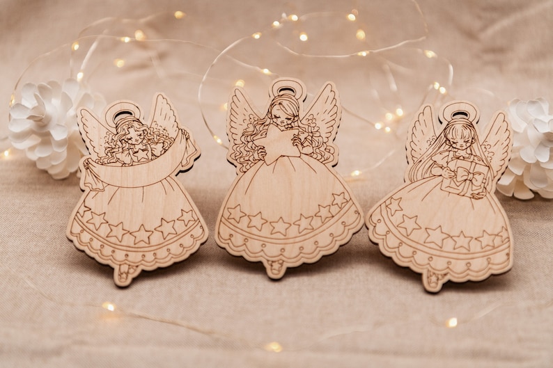 Peut inclure: Trois d&eacute;corations d'anges en bois avec des ailes, des halos et des d&eacute;tails en forme d'&eacute;toile. Chaque ange tient un objet diff&eacute;rent : une &eacute;toile, un rouleau et un coffret cadeau.