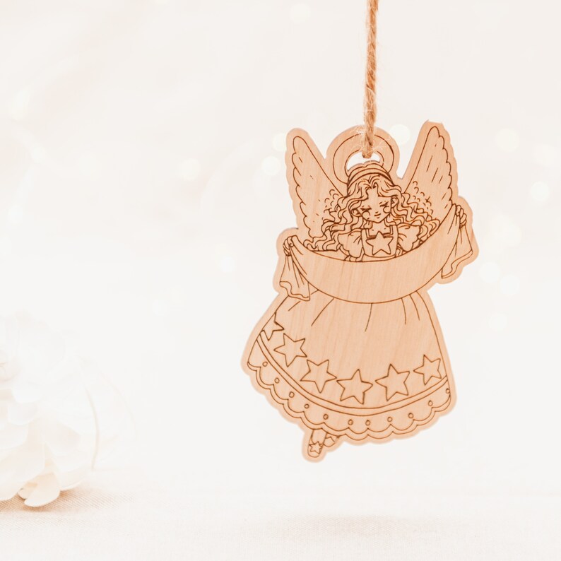 Peut inclure: Une d&eacute;coration d'ange en bois avec une aur&eacute;ole, des ailes et une robe fluide d&eacute;cor&eacute;e d'&eacute;toiles. L'ange tient une banni&egrave;re &agrave; bord festonn&eacute;.