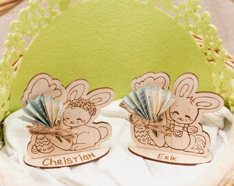 May include: Two wooden bunny figurines with the names "Christian" and "Erik" written below. Each bunny holds a fan of cash and an Easter egg.