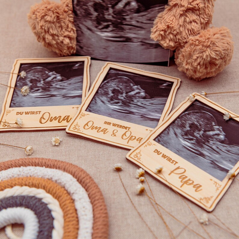 May include: Three wooden photo frames with ultrasound images inside. The frames are decorated with floral designs and have text that reads "Du wirst Oma", "Ihr werdet Oma & Opa", and "Du wirst Papa".
