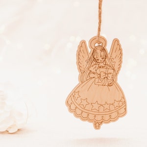 Peut inclure: Une d&eacute;coration d'ange en bois sur fond blanc. L'ange tient une bo&icirc;te cadeau avec un n&oelig;ud. La d&eacute;coration est suspendue &agrave; une ficelle.