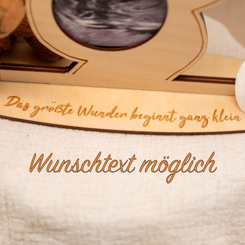May include: A wooden photo frame with a cutout design, holding a sonogram image. The frame has engraved text that reads "Das gr&ouml;&szlig;te Wunder beginnt ganz klein" and "Wunschtext m&ouml;glich".