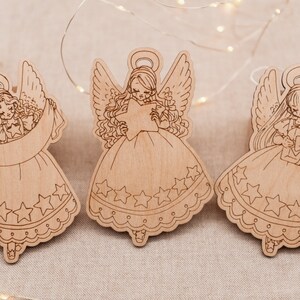 Peut inclure: Trois d&eacute;corations d'ange en bois avec un motif d'&eacute;toile. Chaque ange tient une &eacute;toile et a une aur&eacute;ole. Les anges sont peints dans une couleur bois clair.