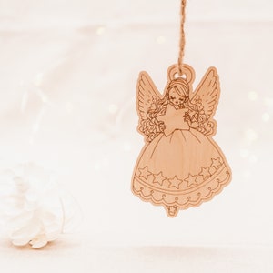 Peut inclure: Une d&eacute;coration d'ange en bois avec une &eacute;toile dans les mains. L'ange porte une robe avec des &eacute;toiles et une bordure en dentelle. La d&eacute;coration est suspendue &agrave; une ficelle.