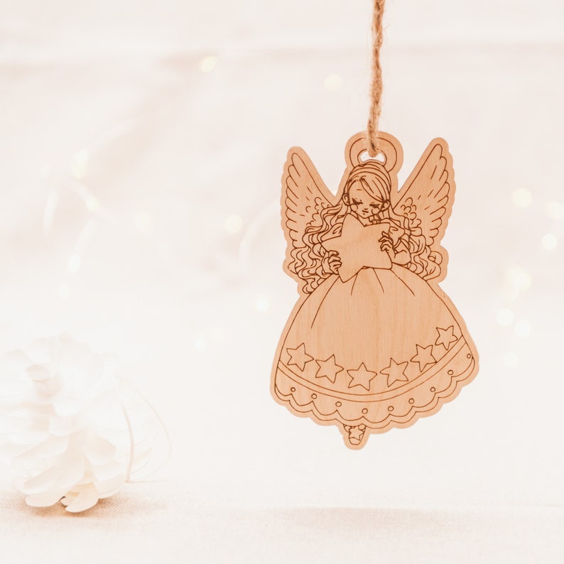 Peut inclure: Une d&eacute;coration d'ange en bois avec une &eacute;toile dans les mains. L'ange porte une robe avec des &eacute;toiles et une bordure en dentelle. La d&eacute;coration est suspendue &agrave; une ficelle.