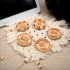 May include: Five wooden tokens with different screen time limits for kids. The tokens are round and have a brown wood finish. The text on the tokens includes "Cassandra's Tablet", "25 Minutes", "Erik's Cartoons", "1 Folge", "Screen Time", and "5 Minutes".