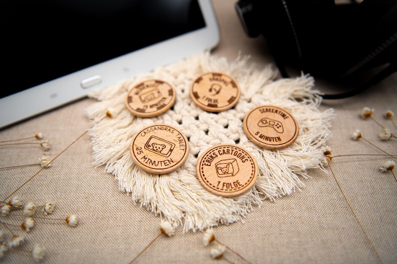 May include: Five wooden tokens with different screen time limits for kids. The tokens are round and have a brown wood finish. The text on the tokens includes "Cassandra's Tablet", "25 Minutes", "Erik's Cartoons", "1 Folge", "Screen Time", and "5 Minutes".