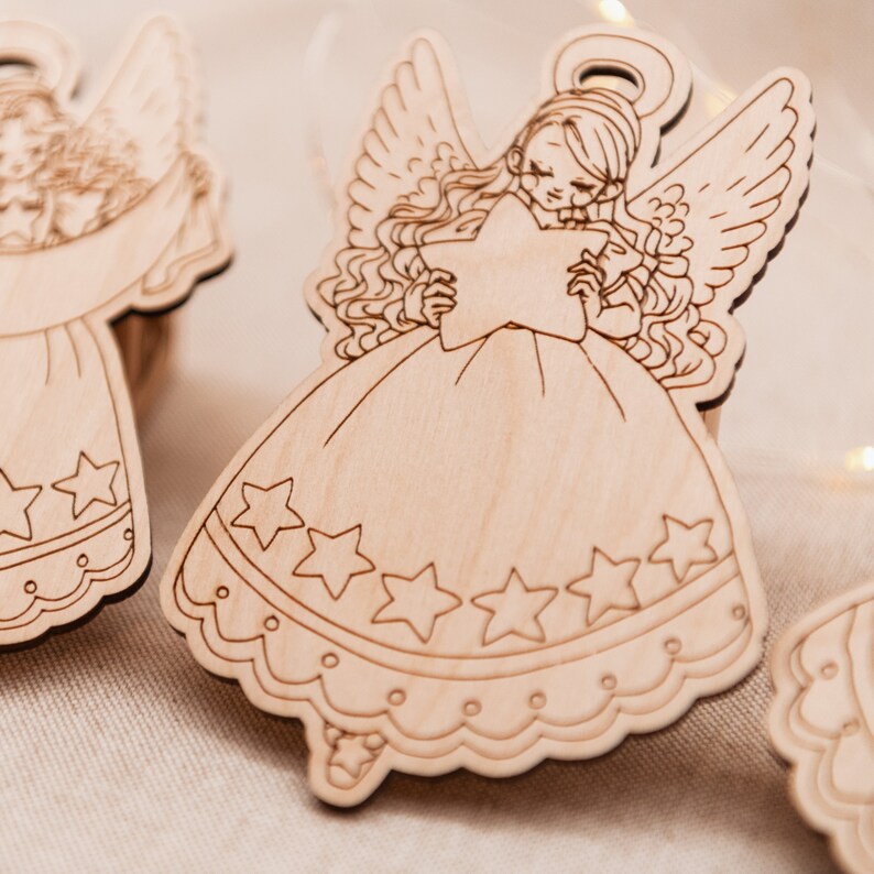Peut inclure: Une d&eacute;coration d'ange en bois avec une aur&eacute;ole, des ailes et une &eacute;toile dans les mains. L'ange porte une robe avec un ourlet festonn&eacute; et des &eacute;toiles autour du bas.