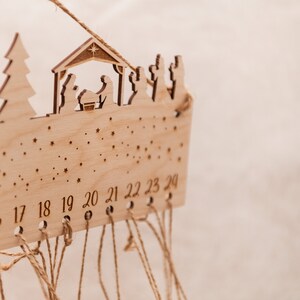 May include: A wooden advent calendar with a nativity scene design. The calendar has 24 numbered slots with twine strings hanging from each slot. The numbers 17 through 24 are visible.