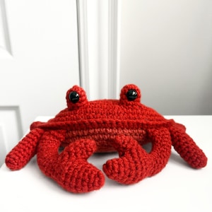 Pode incluir: Um caranguejo vermelho de crochê feito à mão com olhos de segurança pretos. O caranguejo tem uma aparência detalhada e texturizada, com garras e pernas. Este brinquedo de pelúcia é um item artesanal e caprichoso.