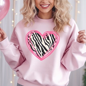 May include: A light pink sweatshirt with a pink outlined heart graphic featuring a zebra print pattern.