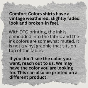 Puede incluir: Un fondo de papel texturizado de color blanco roto con texto negro que explica que las camisas Comfort Colors tienen un aspecto vintage, desgastado, ligeramente deste&ntilde;ido y una sensaci&oacute;n de uso. La impresi&oacute;n DTG integra la tinta en la tela.