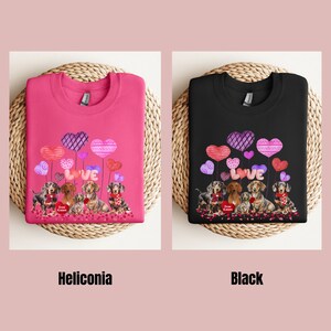 May include: Two sweatshirts, one pink and one black, each with a design of dachshunds, heart-shaped balloons, and the word "LOVE." The pink sweatshirt is labelled "Heliconia," and the black one is labelled "Black."