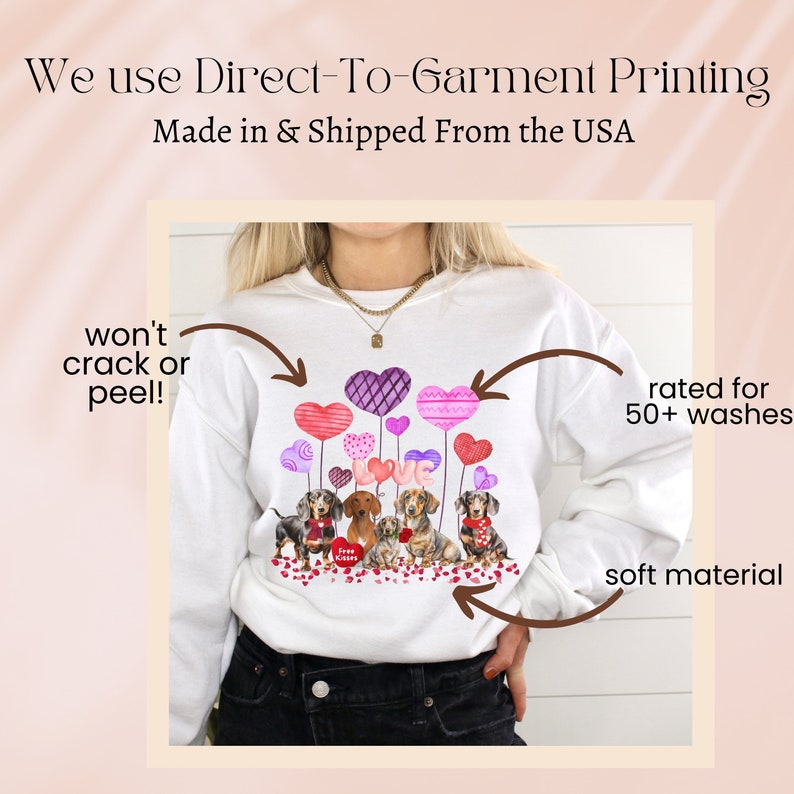 May include: White sweatshirt with a graphic of dachshunds and heart-shaped balloons. The word "LOVE" is displayed. The text "We use Direct-To-Garment Printing" is at the top. The sweatshirt is made of soft material and is rated for 50+ washes.