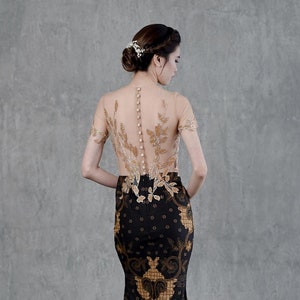 Op de afbeelding: Een zwarte en gouden jurk in zeemeermin-stijl met een doorschijnend, parelversierd lijfje. De jurk heeft een bloemenpatroon en de tekst "Xa Verana F781".