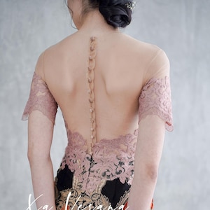 May include: A sheer, nude dress with a pink lace overlay and a button-up back. The dress has a black and gold batik print skirt with the text "Xa Verana F822" on the bottom.