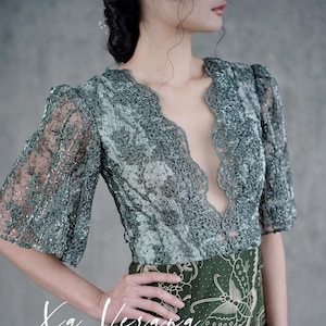 May include: A green lace top with a deep V-neckline and a matching skirt with a butterfly print. The skirt is made of a green and white fabric with a floral pattern. The text "Xa Verana F848" is printed on the bottom of the image.