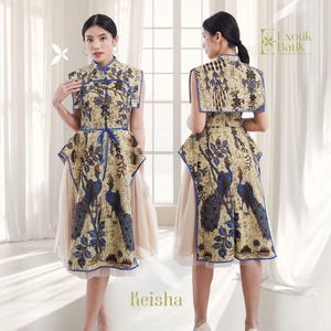 May include: A beige and blue patterned dress with a mandarin collar and a matching cape. The dress features a peacock design and a blue tie belt. The text "Keisha" is visible at the bottom of the image. The brand logo "Exotik Batik" is also visible.