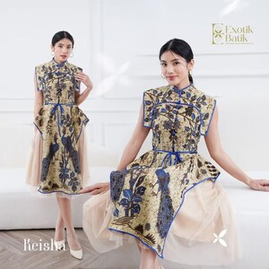 May include: A beige and blue batik dress with a peacock design. The dress has a mandarin collar, cap sleeves, and a blue waist tie. The skirt is layered over a beige tulle underskirt. The dress is from the brand Exotik Batik.