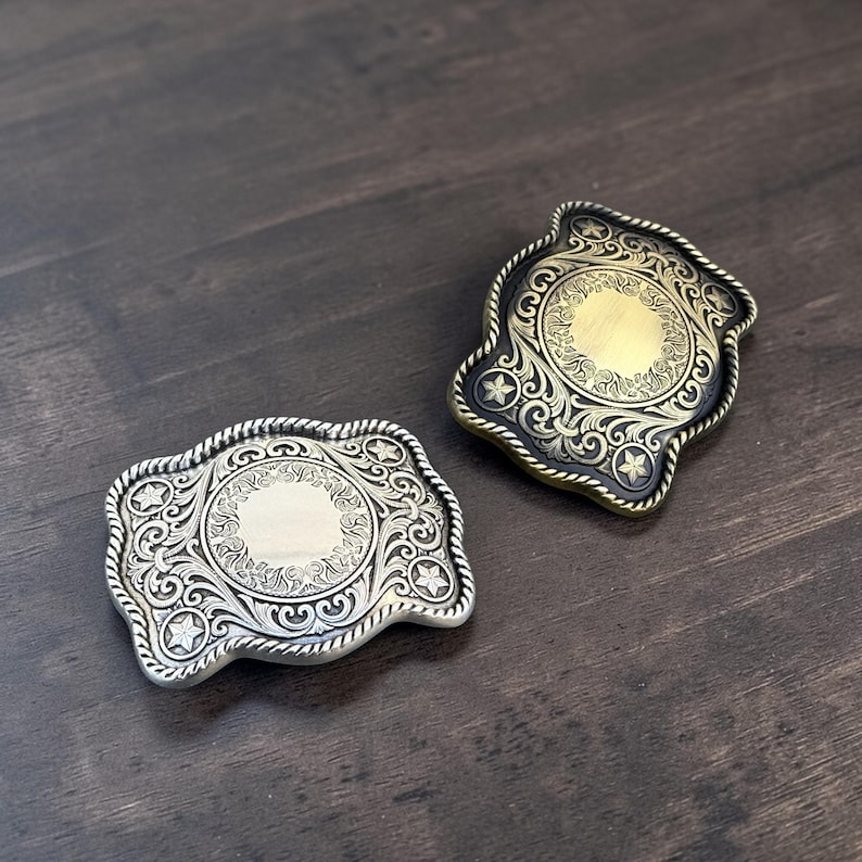 May include: Two decorative belt buckles with ornate scrollwork and star accents. One buckle is silver-toned, the other is gold-toned with a black border. Both have a rope-like edge and a central circular design.