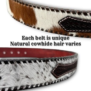May include: Close-up of two cowhide belts. One belt has brown and white hair, the other has white and black hair. Both belts have a dark brown leather backing and black stitching. The text "Each belt is unique Natural cowhide hair varies" is visible.