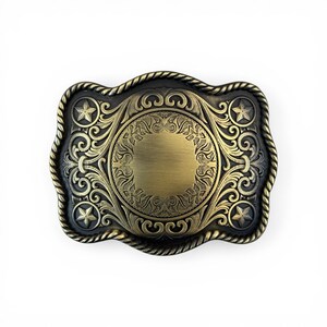 May include: A rectangular, antique-style belt buckle with a detailed design. The buckle features a central circular area surrounded by ornate scrollwork, stars, and a rope-like border. The color is a mix of bronze and black.