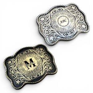 May include: Two decorative metal belt buckles. One is silver with the initials "ABC" and the other is gold with the initial "M" and the name "Michael". Both buckles have a detailed floral and star design.