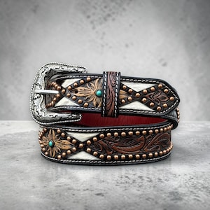 May include: A decorative leather belt with a silver buckle. The belt features a floral design with copper studs and turquoise accents. The belt has a white and brown pattern and a red interior.