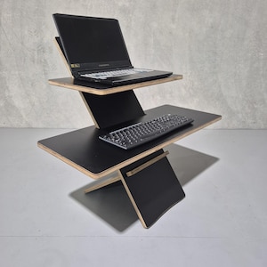 Könnte beinhalten: Ein schwarzer Stehpult mit zwei Ebenen. Die obere Ebene hat einen schwarzen Laptop darauf und die untere Ebene eine schwarze Tastatur. Der Schreibtisch ist aus Holz und hat ein modernes Design.