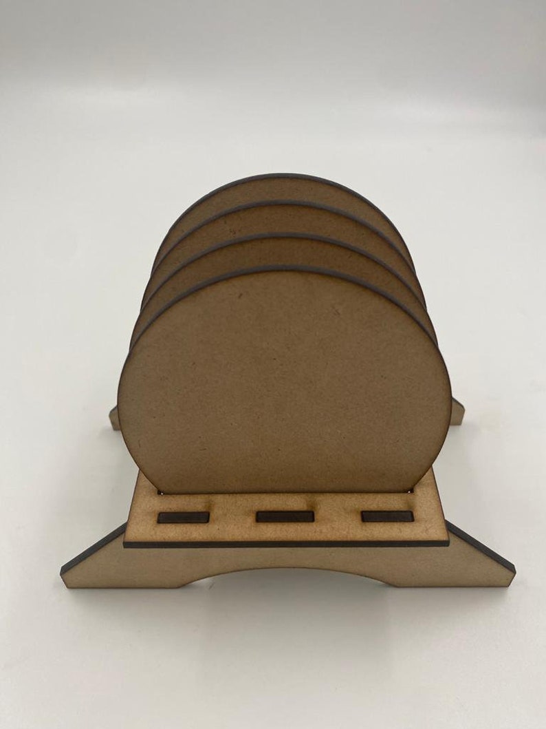 May include: A set of four unfinished wooden coasters with a wooden stand. The coasters are round and have a smooth surface. The stand has a simple design with four legs and a flat top.