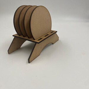 May include: Set of four unfinished wooden coasters with a wooden stand. The coasters are round and have a natural wood color.