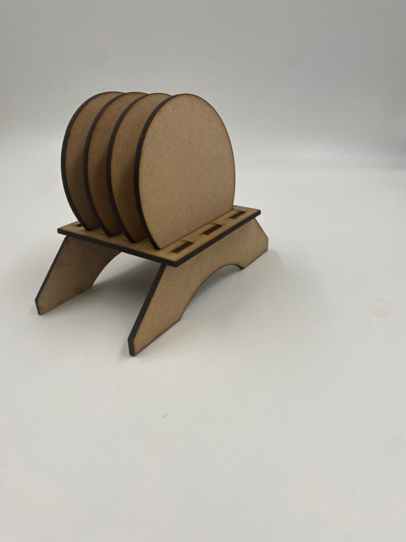 May include: Set of four unfinished wooden coasters with a wooden stand. The coasters are round and have a natural wood color.