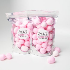 May include: Two silver bags filled with pink freeze-dried salt water taffy. The bags have labels that say "Snoep's Freeze Dried Bubble Gum Salt Water Taffy".