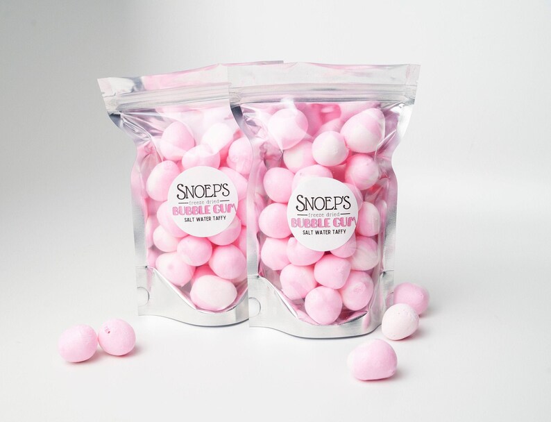 May include: Two silver bags filled with pink freeze-dried salt water taffy. The bags have labels that say "Snoep's Freeze Dried Bubble Gum Salt Water Taffy".