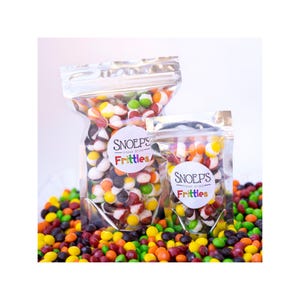 May include: Two bags of freeze-dried candy called "Snoop's Frittles" with a rainbow logo. The bags are filled with colorful, round candies. The candies are scattered on a white surface.