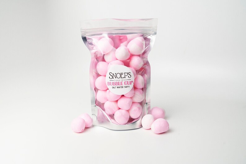 May include: A silver resealable bag filled with pink bubble gum. The bag has a white label with the text "Snoep's - cream soda - Bubble Gum - Salt Water Taffy".