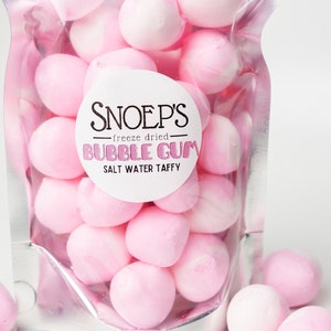 May include: A clear plastic bag filled with pink freeze-dried bubble gum salt water taffy. The bag has a white label with the text "Snoep's - freeze dried - Bubble Gum Salt Water Taffy".