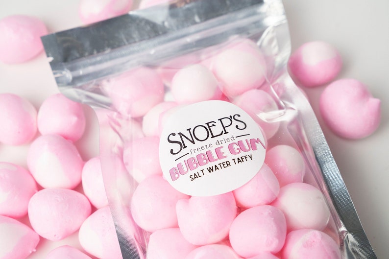 May include: A clear plastic bag filled with pink and white freeze-dried bubble gum. The bag has a label that reads "Snoep's - freeze dried - Bubble Gum - Salt Water Taffy".