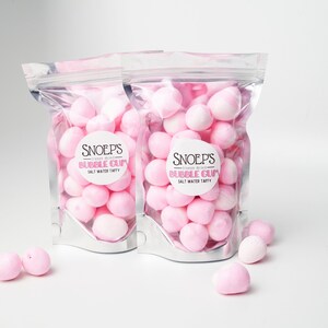 May include: Two clear plastic bags filled with pink bubble gum candies. The bags have a white label with the text "Snoep's" and "Bubble Gum" in black. The bags are on a white surface.