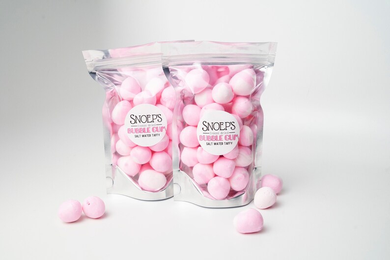 May include: Two clear plastic bags filled with pink bubble gum candies. The bags have a white label with the text "Snoep's" and "Bubble Gum" in black. The bags are on a white surface.