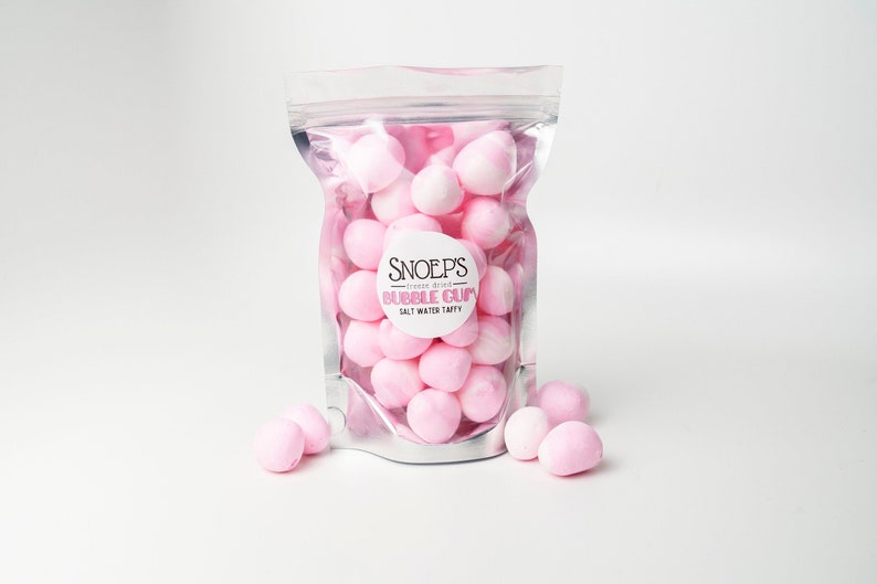 May include: A clear plastic bag filled with pink and white bubble gum. The bag has a white label with the text "Snoep's - freeze dried - Bubble Gum - Salt Water Taffy".