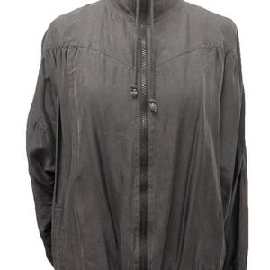 May include: A charcoal gray zip-up jacket with a high collar and elastic cuffs. The jacket has a full-length zipper and a drawstring at the collar. The fabric appears to be lightweight and slightly textured, suitable for layering.