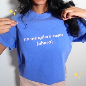 May include: A blue t-shirt with the text "no me quiero casar (ahora)" in white. The shirt is a solid blue color and has short sleeves. The text is centered on the front of the shirt.