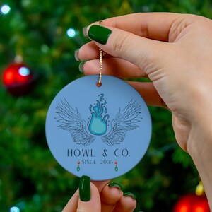 Op de afbeelding: Een blauwe en groene kerstbal met een blauwe vlam en vleugels, en de tekst "HOWL & CO. SINCE 2005".