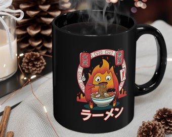 May include: Black ceramic mug with a cartoon illustration of a fire spirit eating ramen noodles. The mug has Japanese text that says "Ramen" and "Fire Demon".
